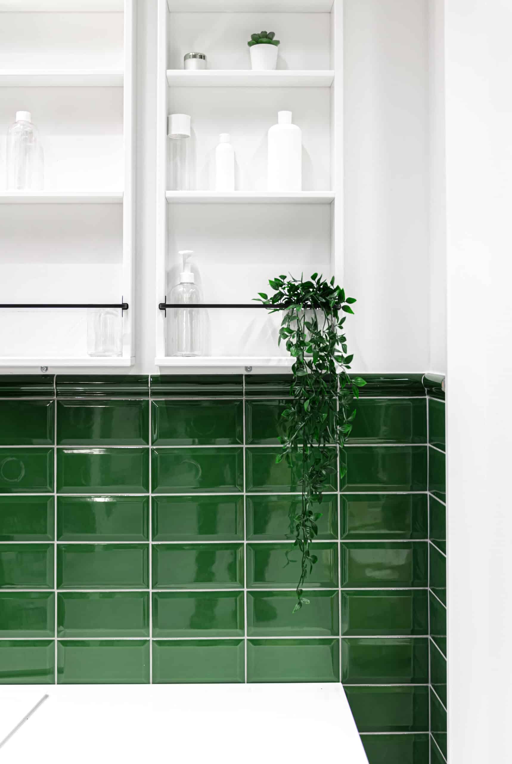 Part of the bathroom interior with green tiles and white cabinets on the wall.